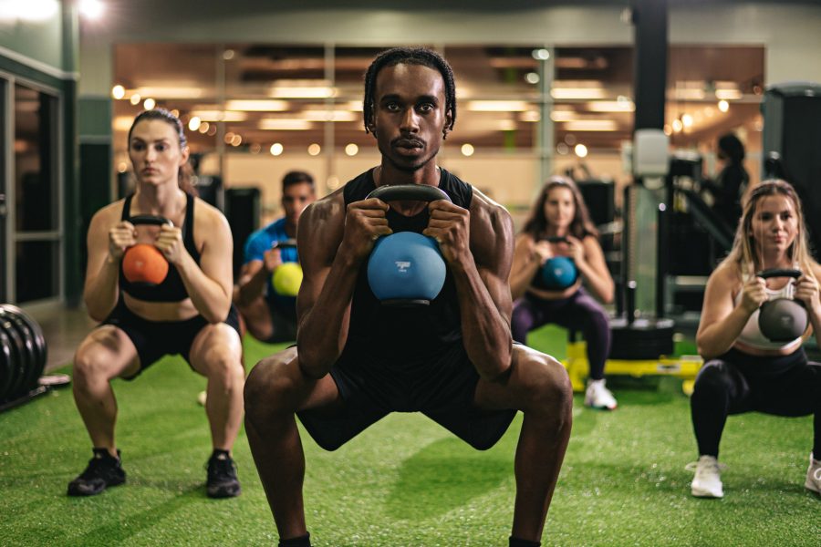 Five people in a gym squatting with kettlebells