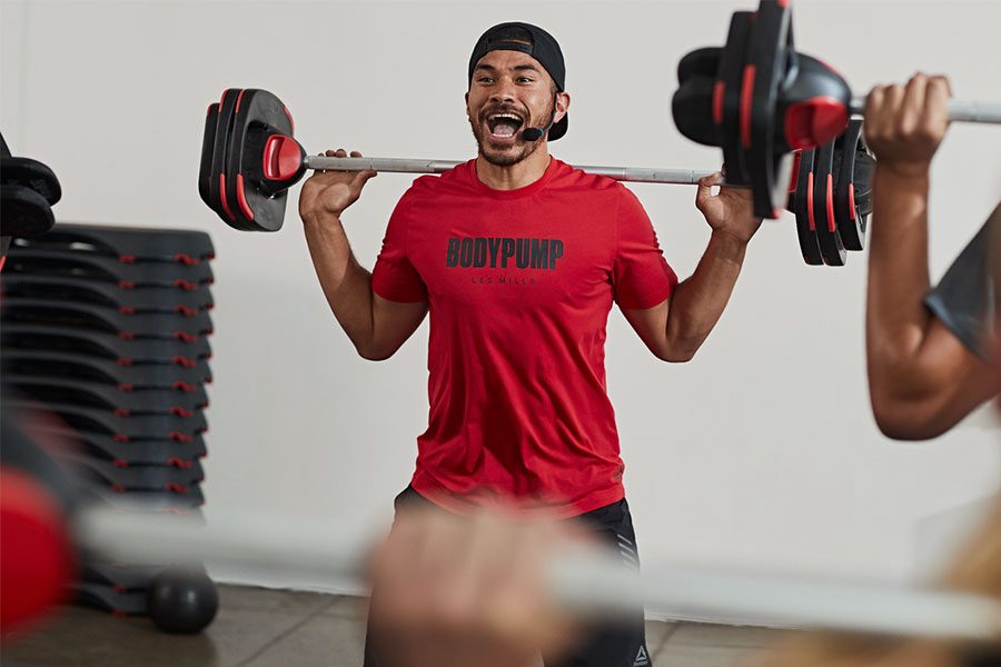 Male instructor with barbell across shoulders teaching a Les Mills BODYPUMP class